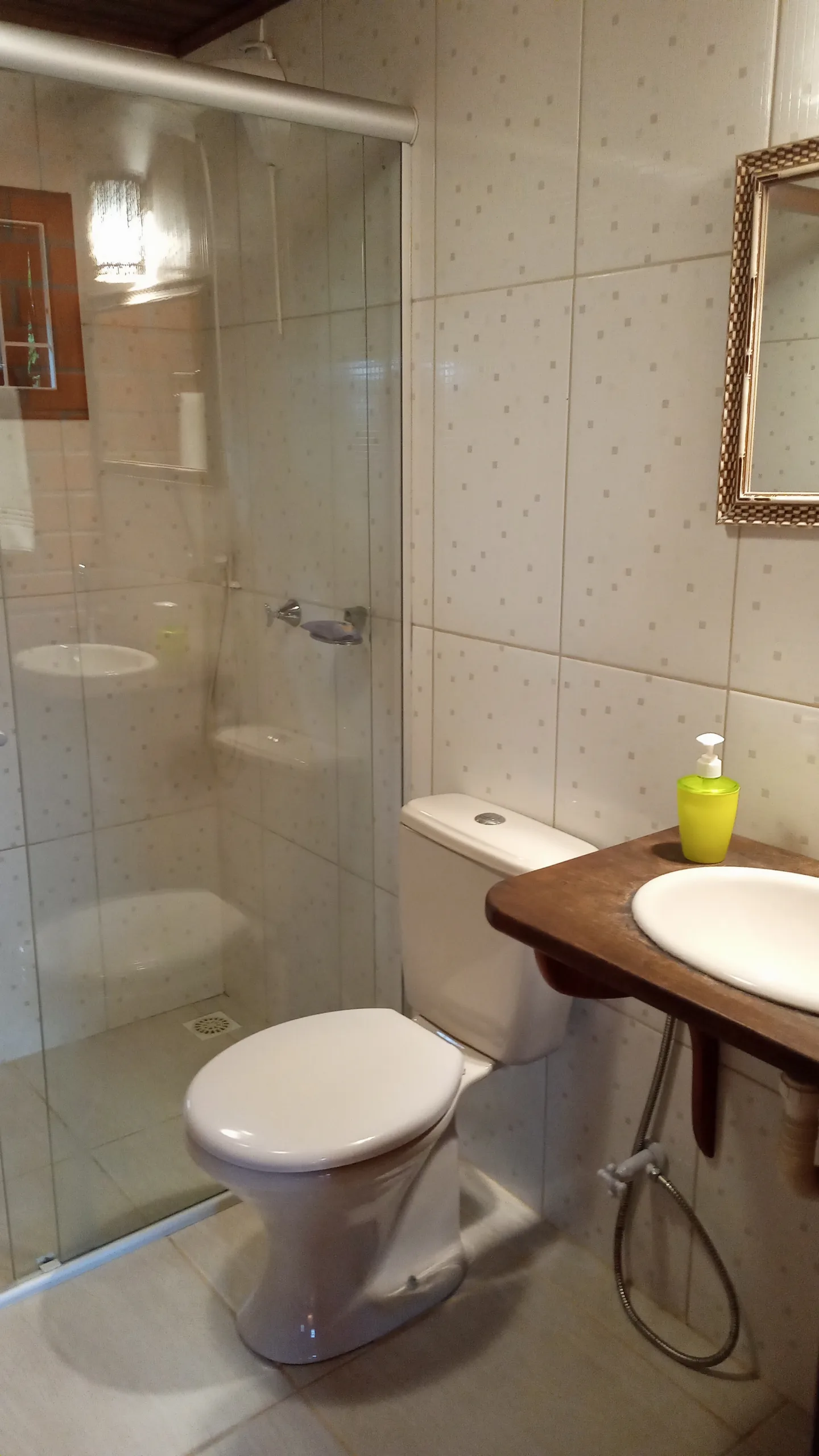 Banheiro do Bungalow 12 com box de vidro, bancada de madeira e espelho