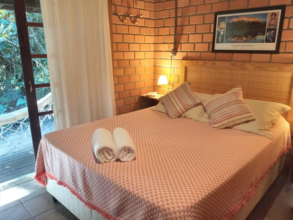 Quarto de casal com abajur aceso e saída para a varanda com rede