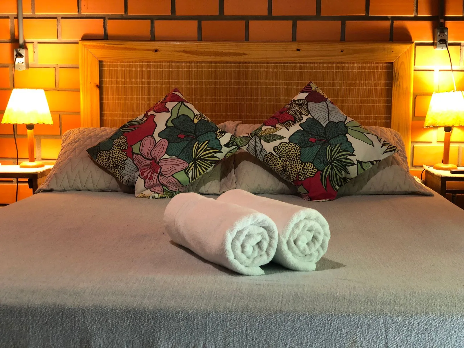 Cama de casal arrumada com almofadas floridas e toalhas, em suíte da Pousada Rosa & Canela