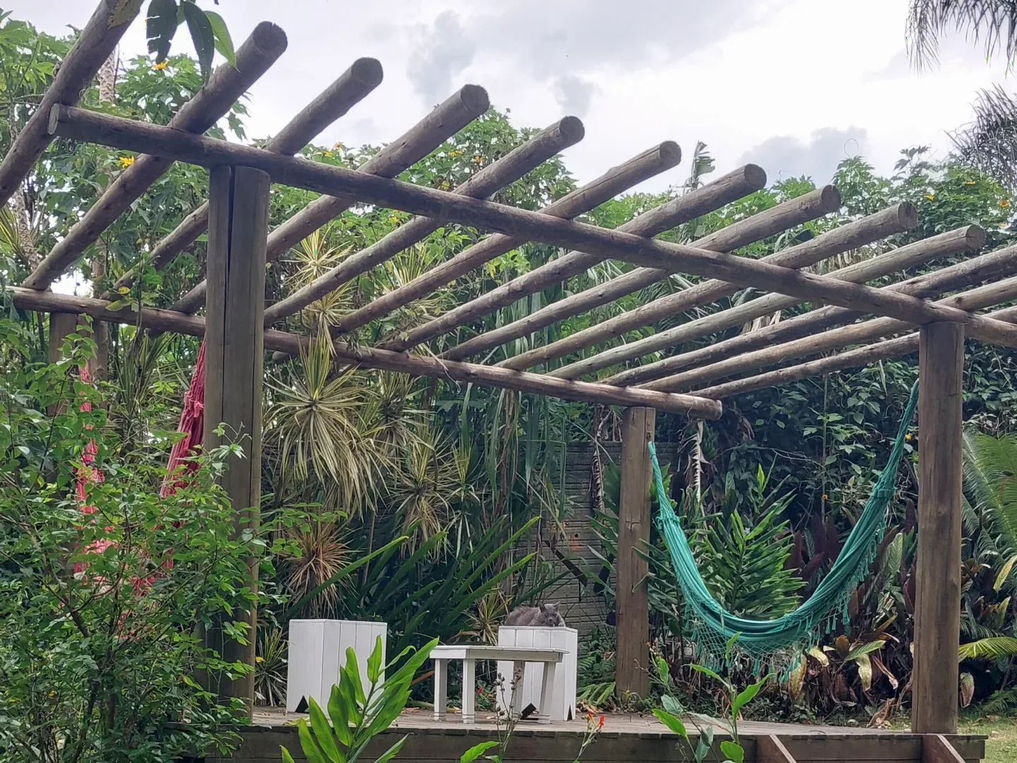 Teto de madeira roliça do pergolado do Espaço Zen sobre o deck com redes e bancos brancos
