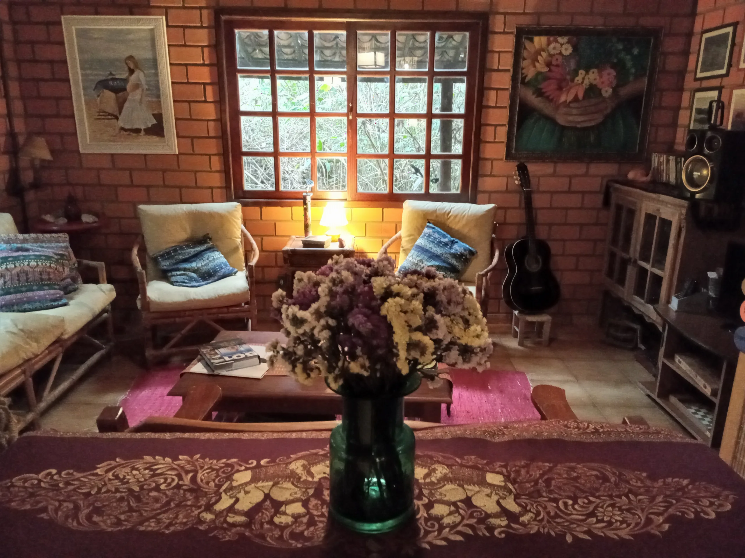 Lounge da pousada com poltronas, almofadas, violão, quadros e vaso de flores
