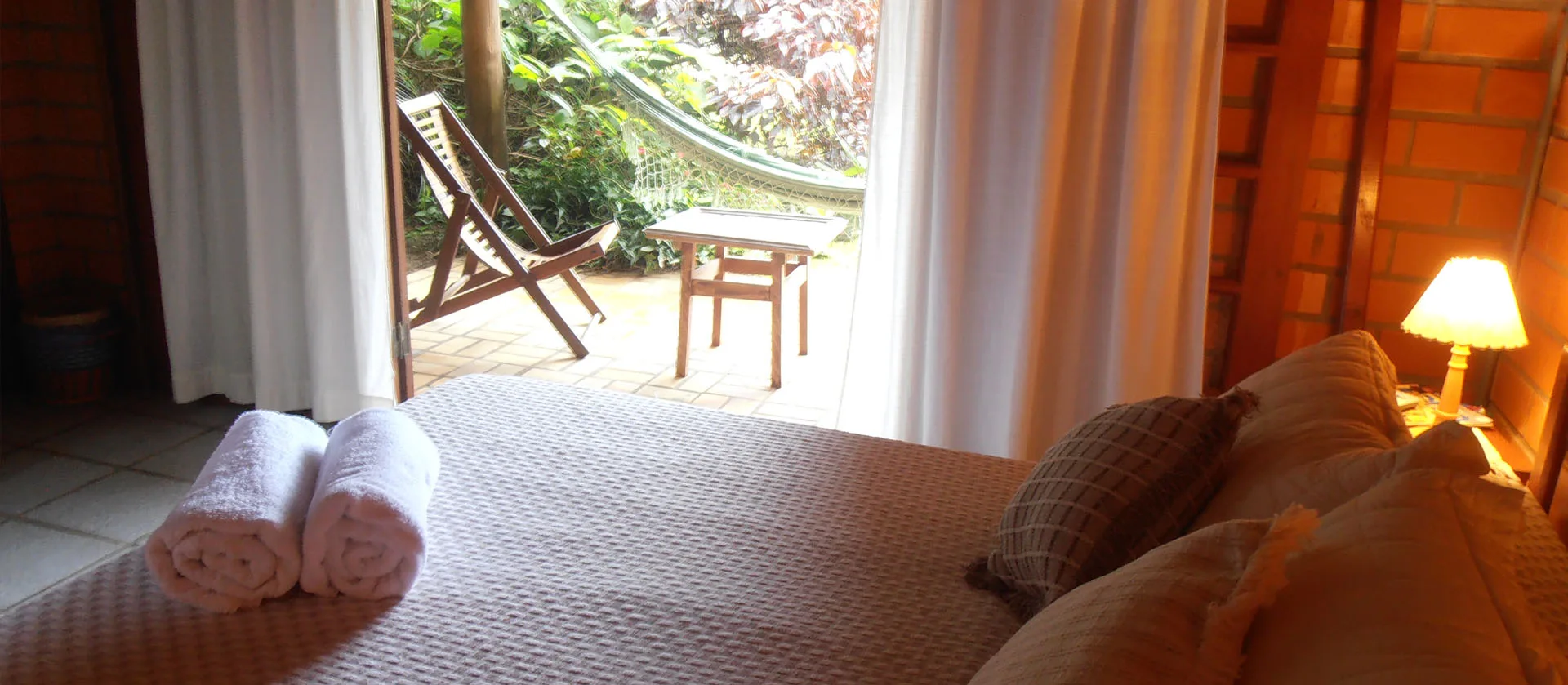 Suíte com cama de casal e porta aberta para a varanda com rede
